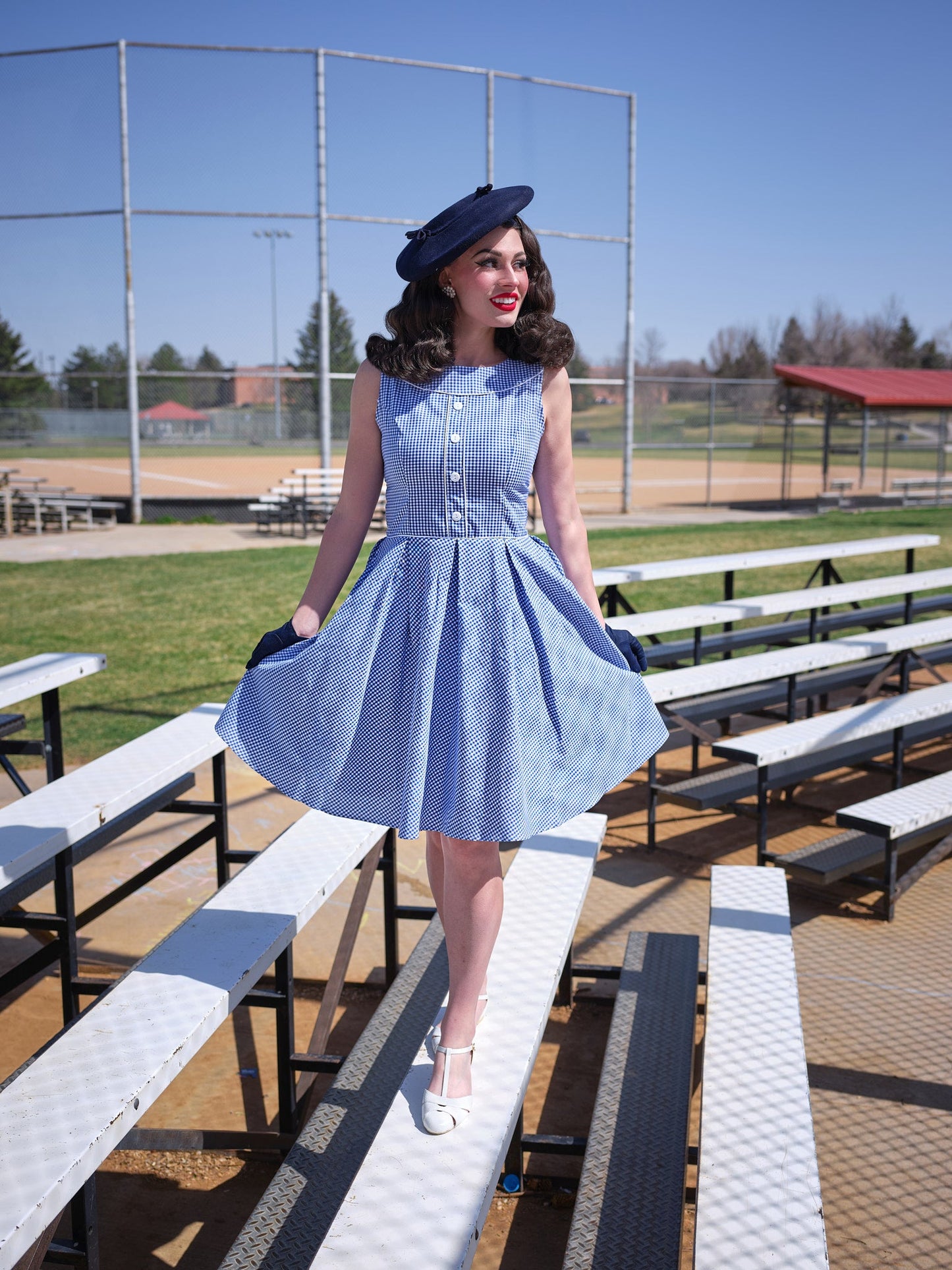 Woman in a light blue gingham dress with a vintage style and wearing a dark straw hat.