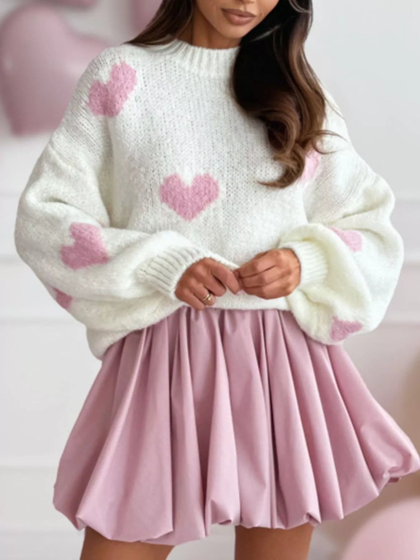 Woman wearing an oversized white fuzzy knit sweater featuring large pink heart patterns and voluminous balloon sleeves.