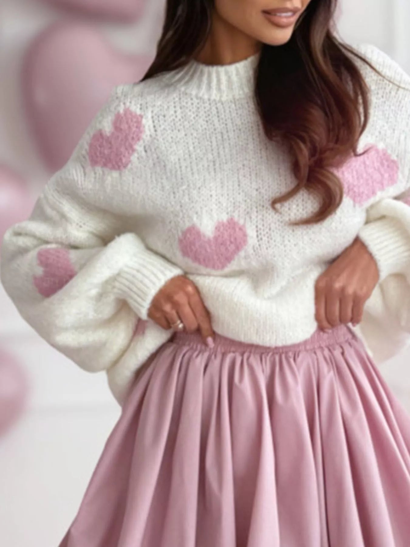 Close-up of the ribbed mock neck and soft knit texture of a white sweater with a pink heart print.