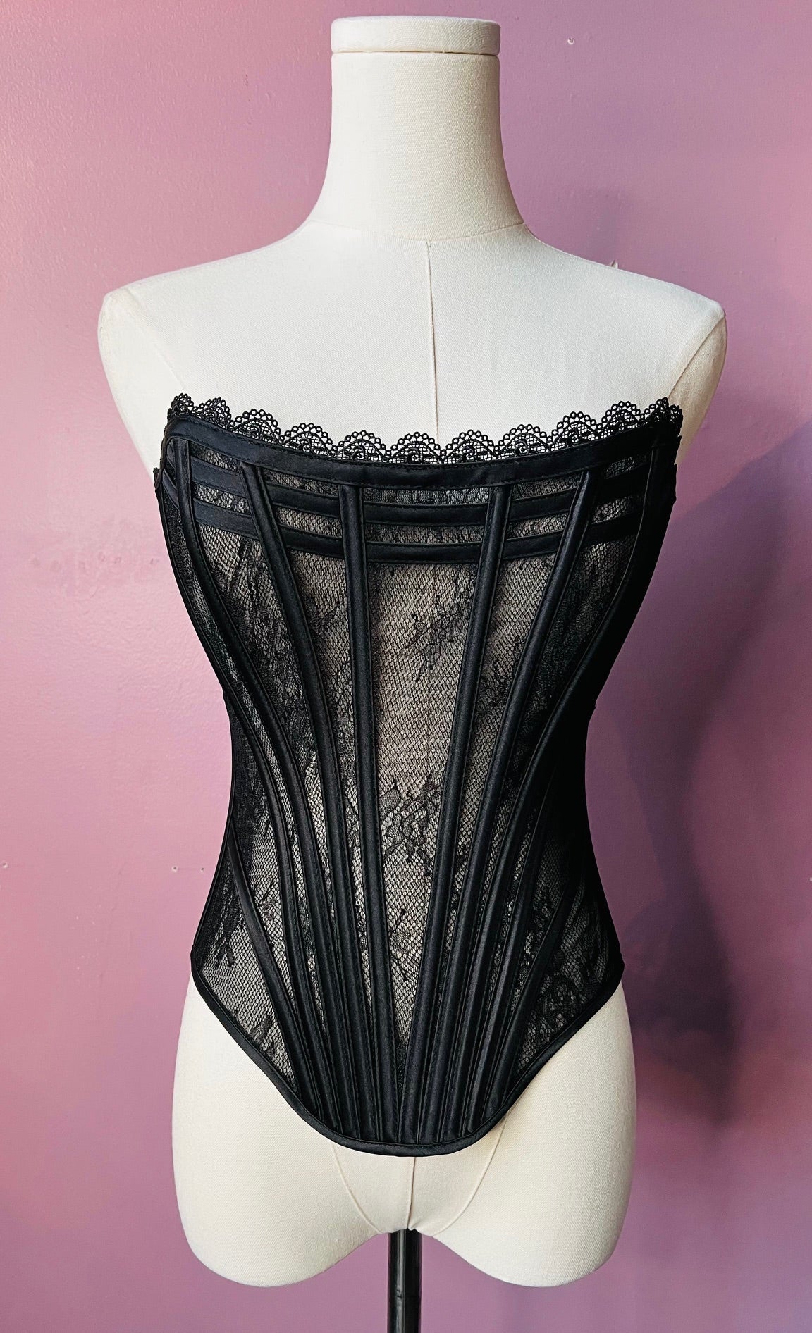 Black lace corset on a mannequin against a pink background