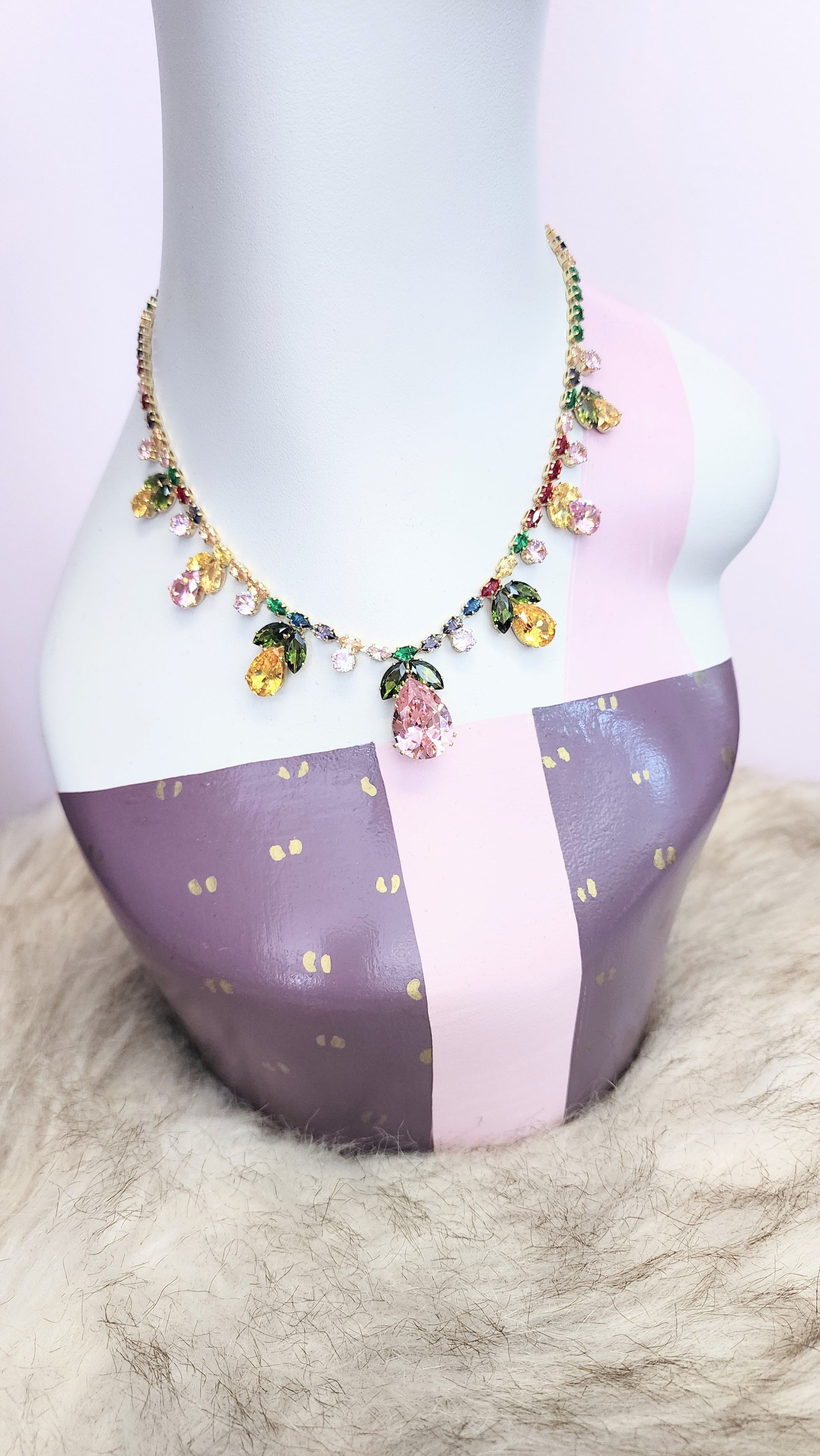 Necklace with pastel rhinestones on a mannequin bust against a pink background