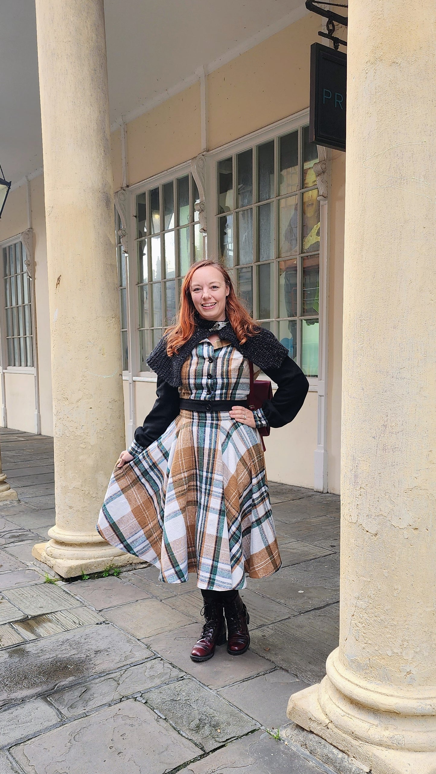 A close-up view of a custom-made plaid flannel and black wool jacket, featuring a cozy hood and vintage-inspired construction. The fabric is a classic tartan pattern in shades of red, green, and navy, perfect for autumn travel.