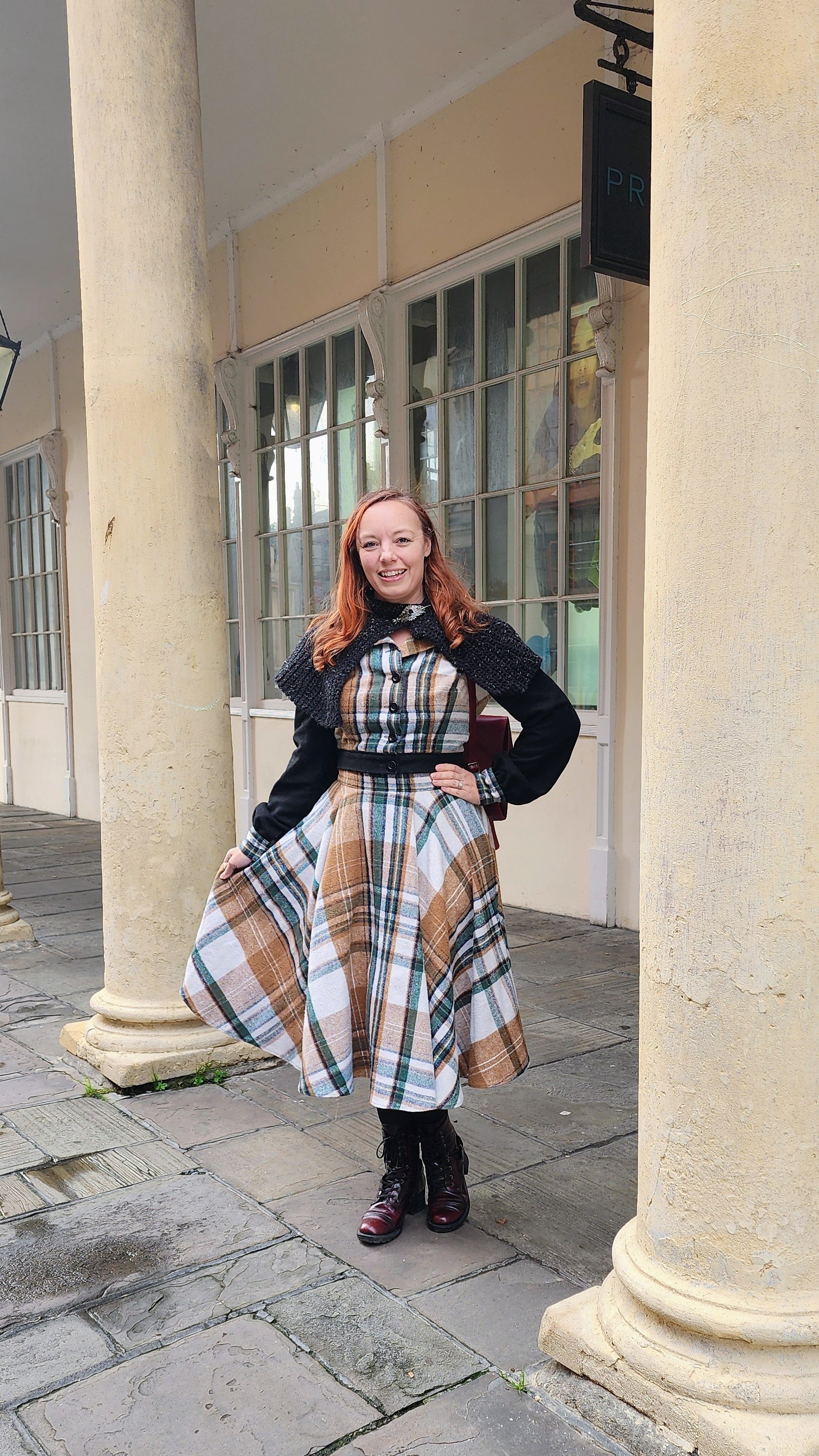 A close-up view of a custom-made plaid flannel and black wool jacket, featuring a cozy hood and vintage-inspired construction. The fabric is a classic tartan pattern in shades of red, green, and navy, perfect for autumn travel.