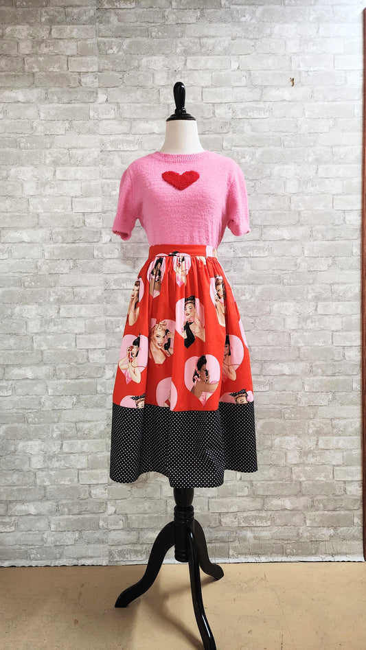Close-up of a handmade red Valentine's Day swing skirt with heart-framed pin-up girl print and black polka dot hem on a mannequin.