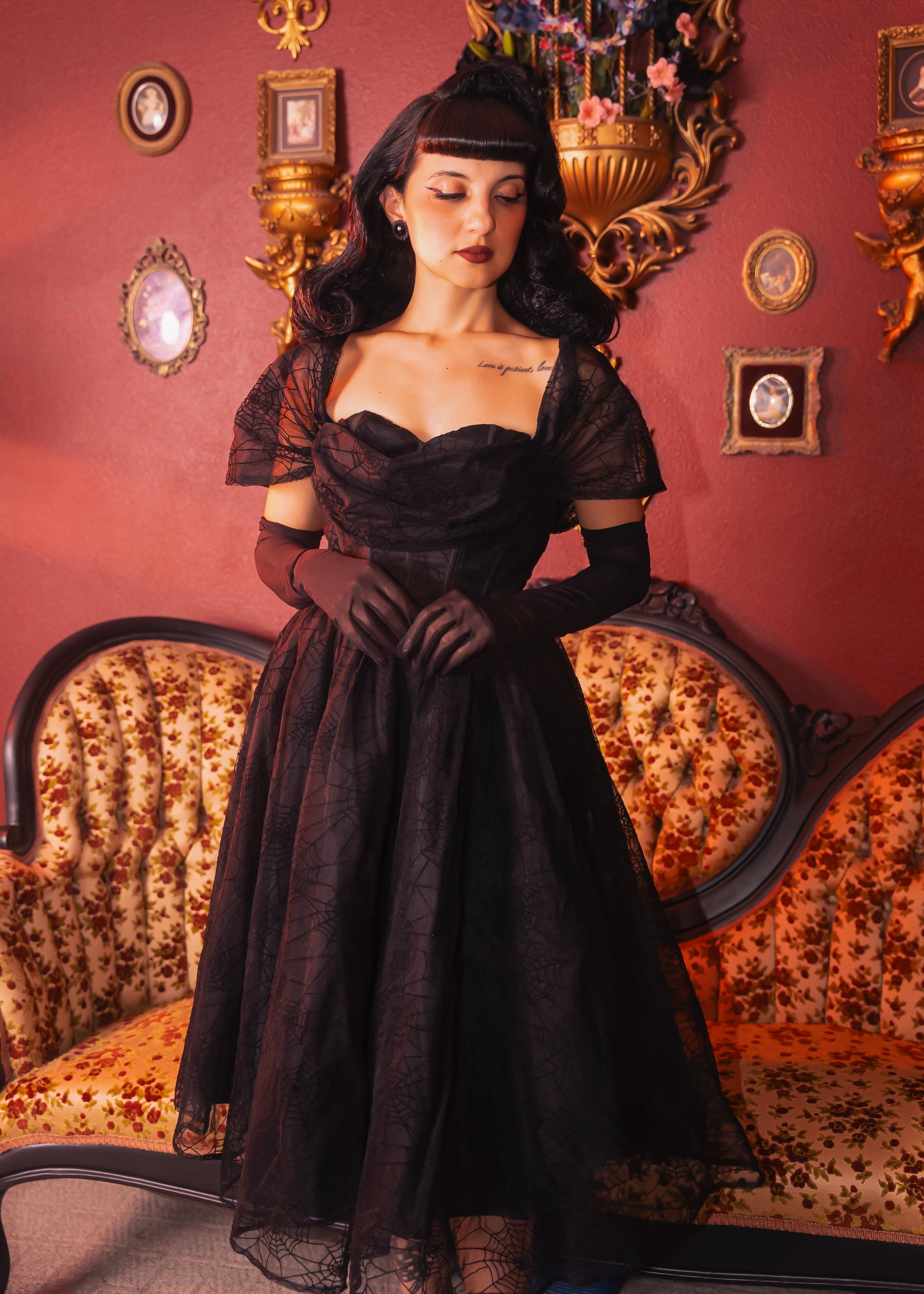 Woman in a black Halloween spiderweb dress standing in an ornate room with decorative wall pieces.